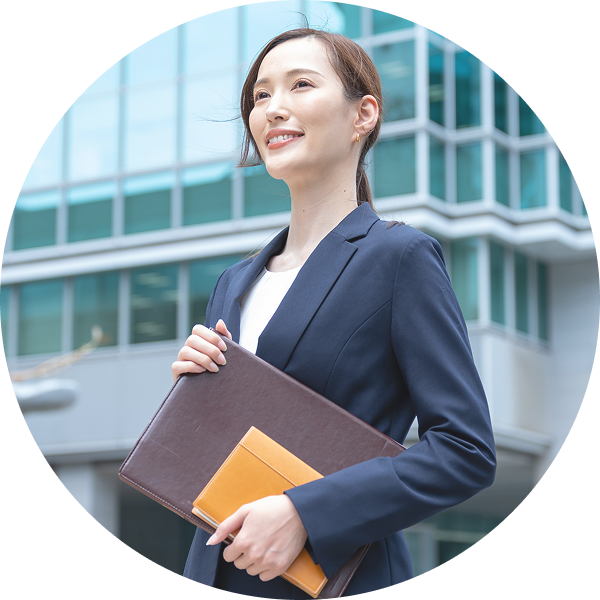 ガラス張りのオフィスビル前で書類ケースを抱え、前向きな表情を見せるスーツ姿の女性